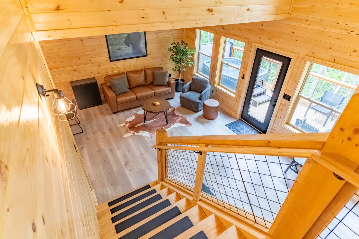 This image captures a cozy corner of the living area with a plush sofa, wooden stairs, a coffee table, and expansive windows that bathe the space in morning sunlight. The ambiance is relaxed and cheerful, ideal for unwinding after a day out.