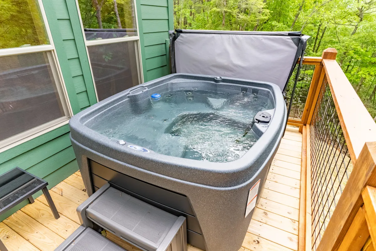 An inviting hot tub set on a wooden deck surrounded by lush greenery. The hot tub is ready for a relaxing soak, offering peaceful views and an atmosphere of tranquil seclusion.