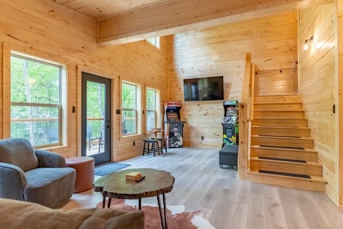 This image captures a lively interior game area featuring wooden stairs, multiple arcade machines, a cozy sofa, and a coffee table. The arrangement suggests a welcoming space for socializing, playing games, and relaxing with friends or family.