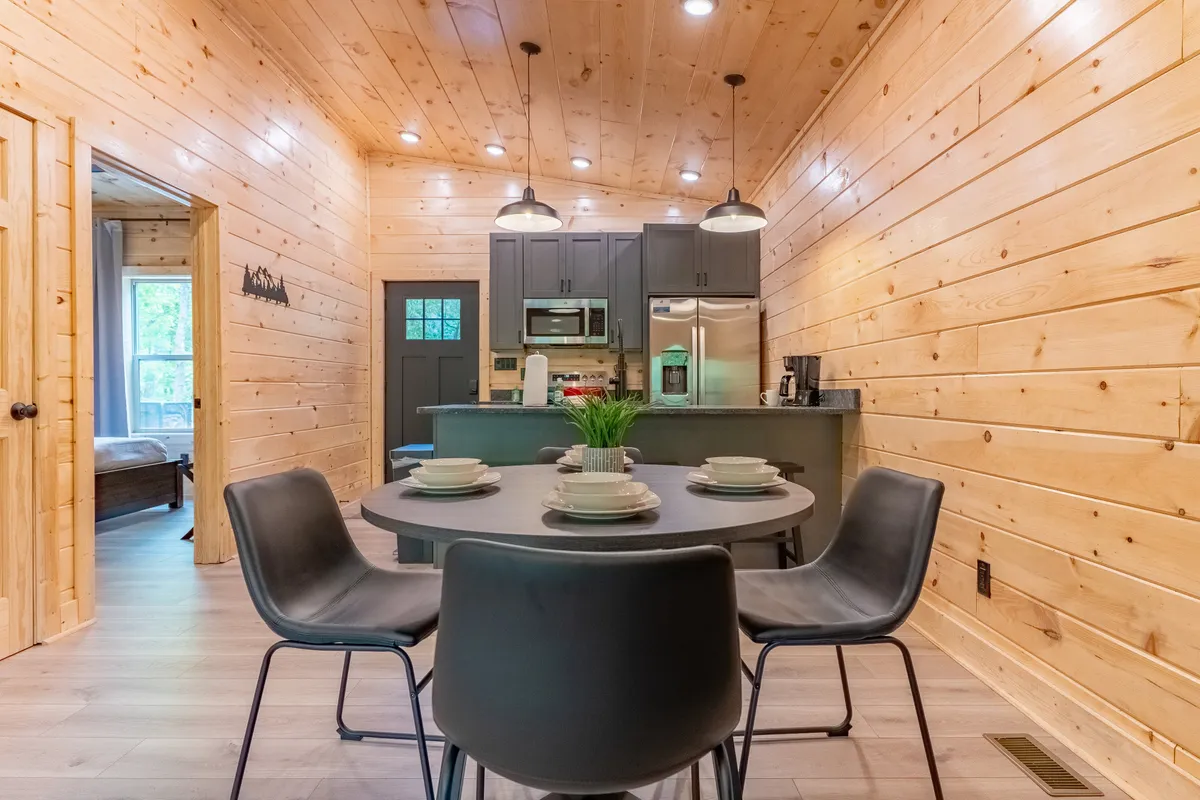 A cozy and modern dining area featuring a round table and kitchen island, set against wooden walls and accented by contemporary appliances. The layout encourages social interaction, shared meals, and storytelling.