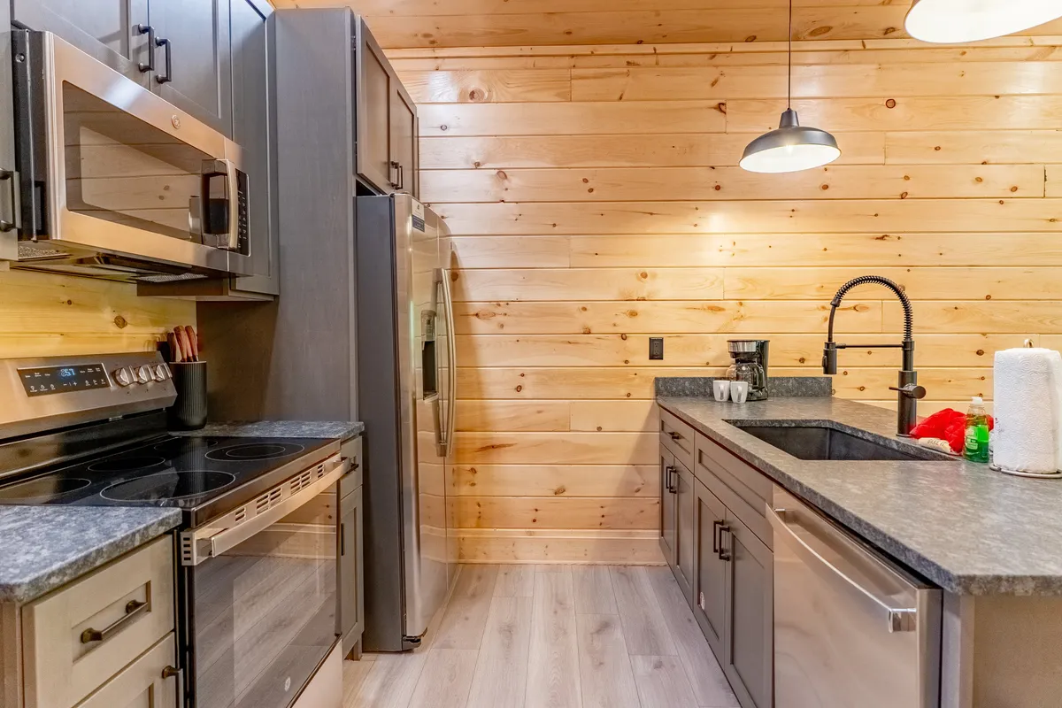 A welcoming, modern kitchen with stainless steel appliances and granite countertops set against warm wooden walls. The space is designed for gathering and cooking, with ample workspace for meal prep and a cozy atmosphere ideal for family or group activities.